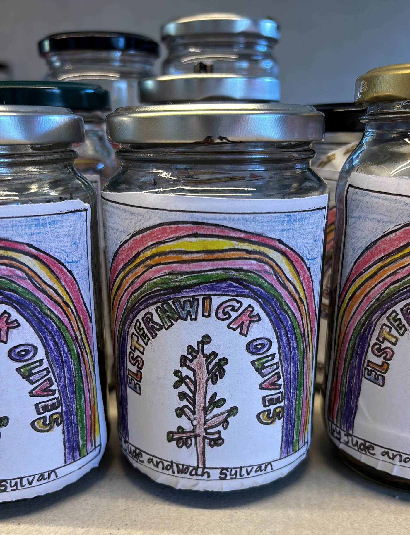 close up of 3 jars of homemade olives with hand-drawn labels on a bench