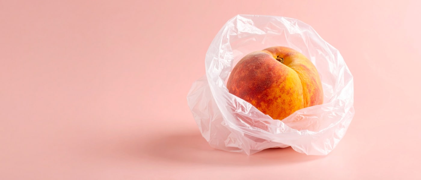 a peach wrapped in single use plastic against a soft pink background