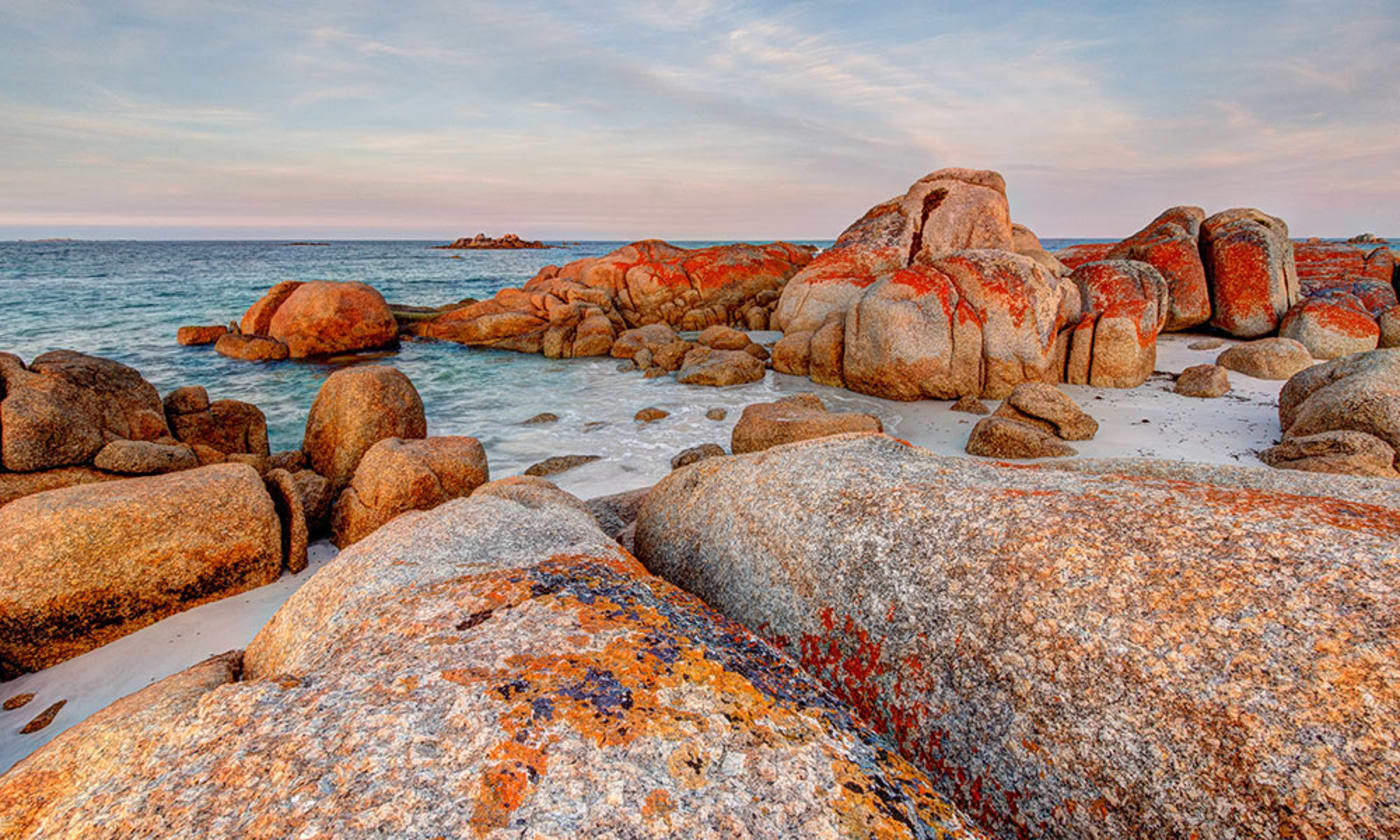 Giant granite rock boulders covered in orange and red lichen at Bay of Fires, Tasmania.