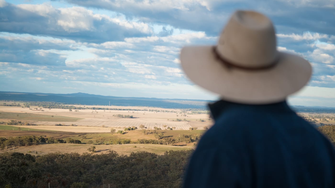 Glenn Morris= general manager of FigTrees Organic Farms= on his organic beef farm near Inverell= NSW. Glen is wearing a dark blue work shirt and brown hat and is looking out over farmland and trees.