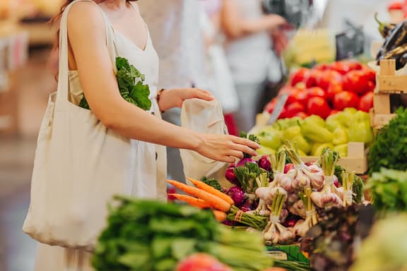 Female hands puts fruits and vegetables in cotton produce bag at food market. Reusable eco bag for shopping. Zero waste concept. Plastic-free alternatives.