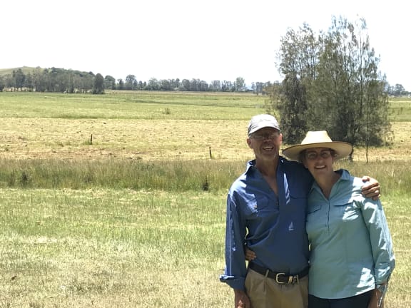 2 people stand with their arms around each other on an agricultural property with grass and trees in the background. Patches Flat, a 68-hectare former sugar cane farm in northern NSW, is being transformed through the Koala Friendly Carbon Initiative project.