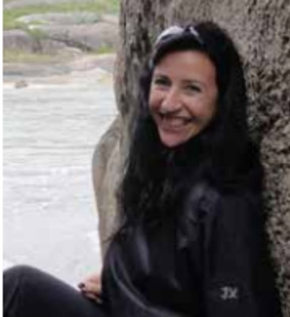 woman sits against tree and smiles at camera