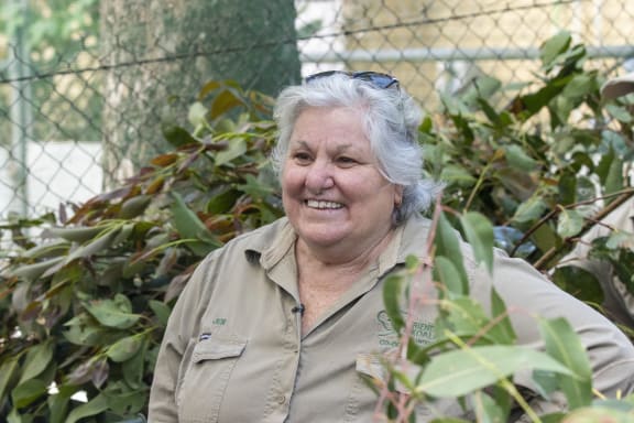 Jen stands in front of piles of eucalyptus branches and smiles at someone behind the camera