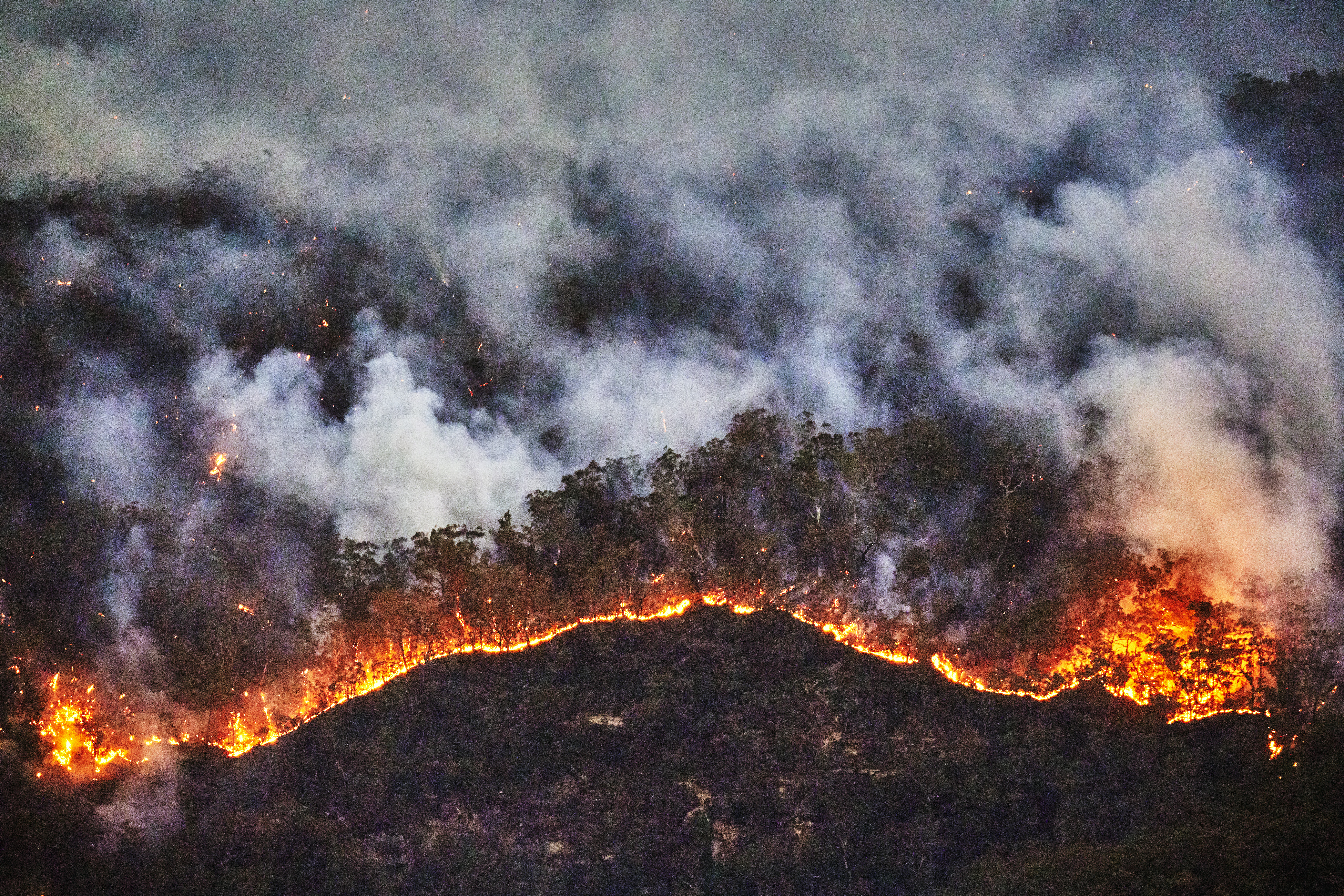 Stock Image. The fire front at night appears as a bright yellow and red jagged line in the dark blue eucalyptus forest in the Jamison Valley. Photograph taken from Echo Point lookout, Katoomba, Blue Mountains